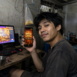 ผู้ใช้งานถือมือถือแสดง Mega Win ขณะเล่นสล็อตบนคอม ภาพประกอบรีวิว TUNDER24HR